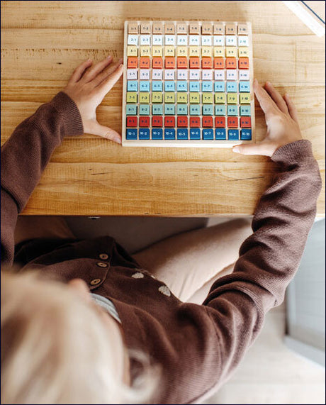 Person hält ein farbiges Zahlenpuzzle mit bunten Steinen auf einem Holztisch.