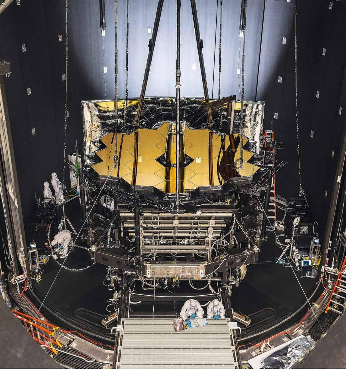 Blick auf einen Teil eines großen wissenschaftlichen Instruments im Labor, mit Technik, Kabeln und Forschern in Schutzkleidung.