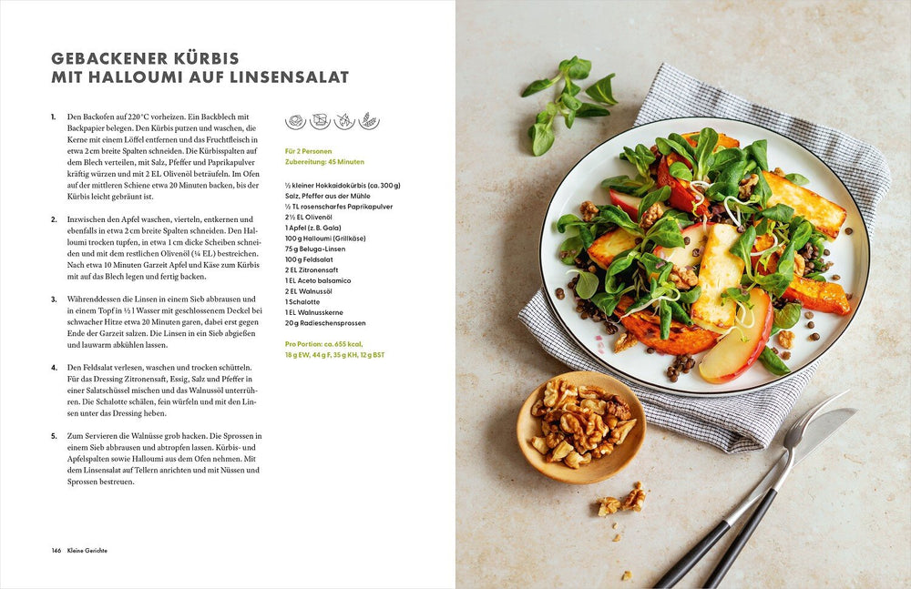 Bunter Salat mit gebackener Kürbis, Halloumi, Apfel, Walnüssen und Linsen auf einem weißen Teller, daneben eine kleine Schale mit
