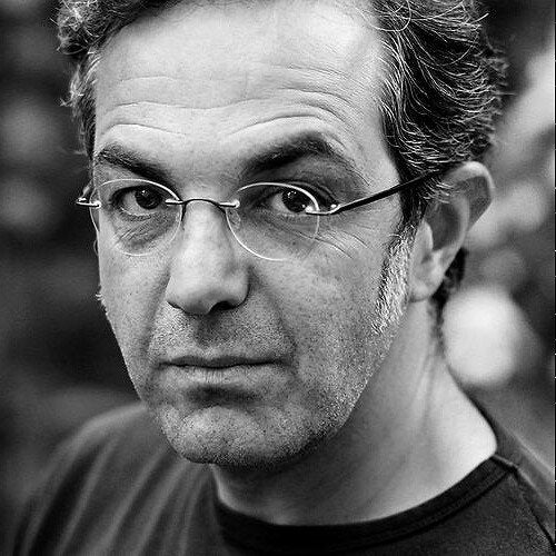 Schwarz-weiß-Porträt eines Mannes mit Brille, kurze Haare und ernstem Blick.