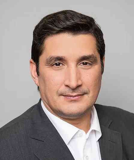 Porträt eines Mannes in Anzug und weißem Hemd vor grauem Hintergrund.