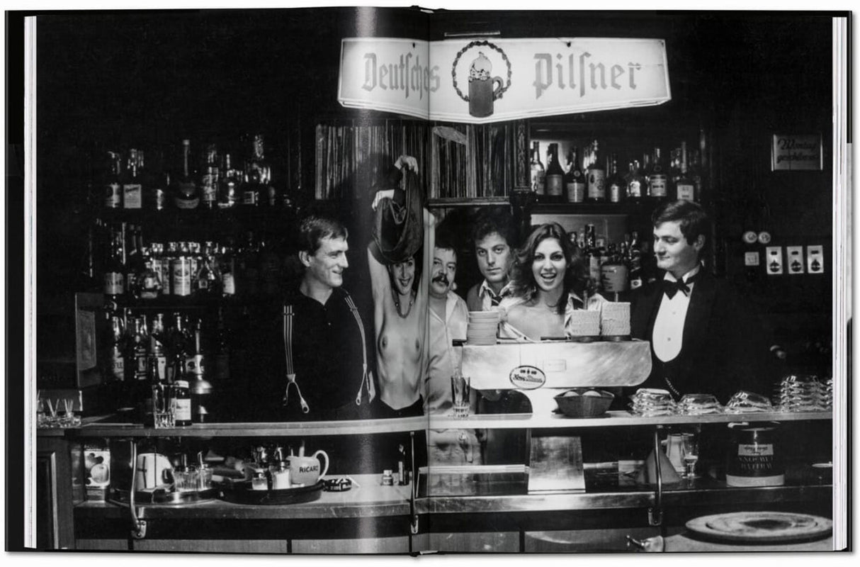 Schwarz-weiß-Foto eines Barpersonals hinter einer Theke mit Getränken, unter einem Schild "Deutsches Pilsner".