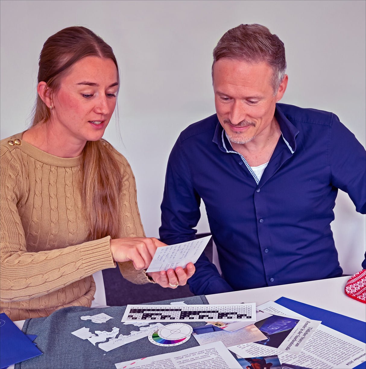 Zwei Personen sitzen an einem Tisch, schauen auf Papiere und Unterlagen, die vor ihnen liegen.