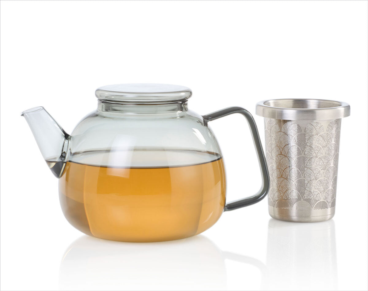 Glas-Kanne mit braunem Tee und Metall-Teefilter auf weißem Hintergrund.