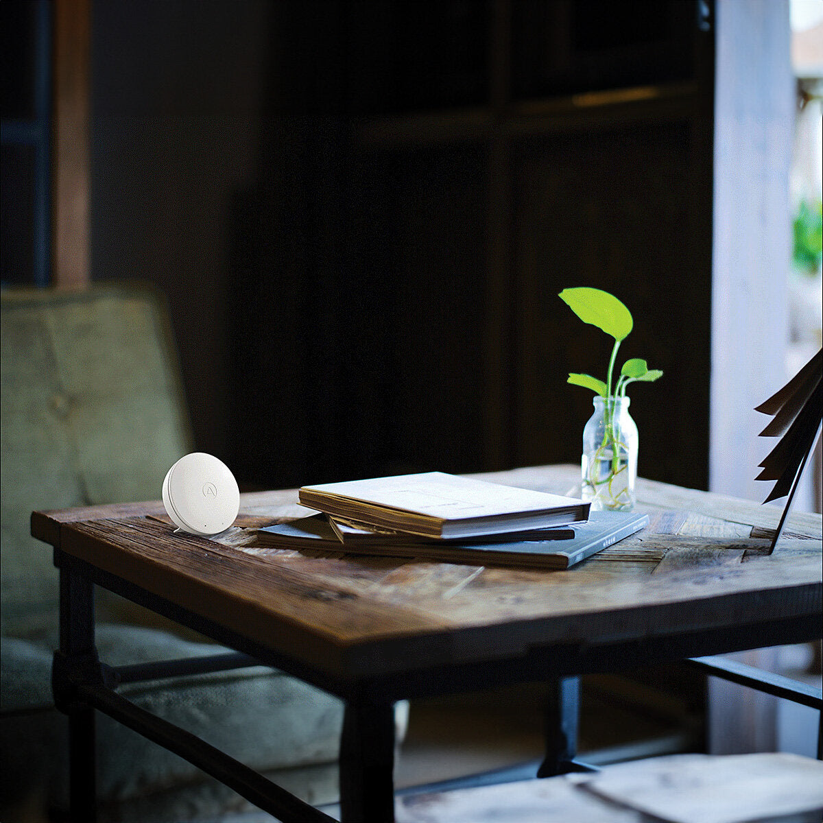 Ein Holztisch mit offenen Büchern, einem Laptop, einer Vase mit grünen Blättern und einem weißen runden Gerät.