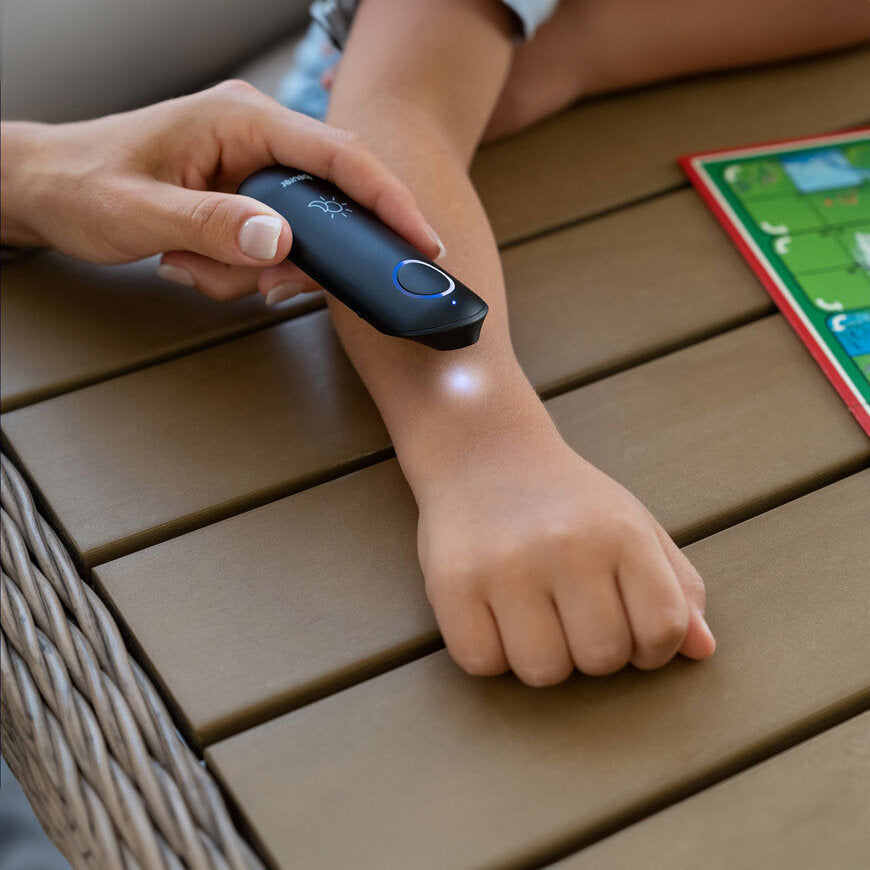 Hand hält Infrarot-Thermometer an Kinderarm, auf Tisch mit Spielbrett.