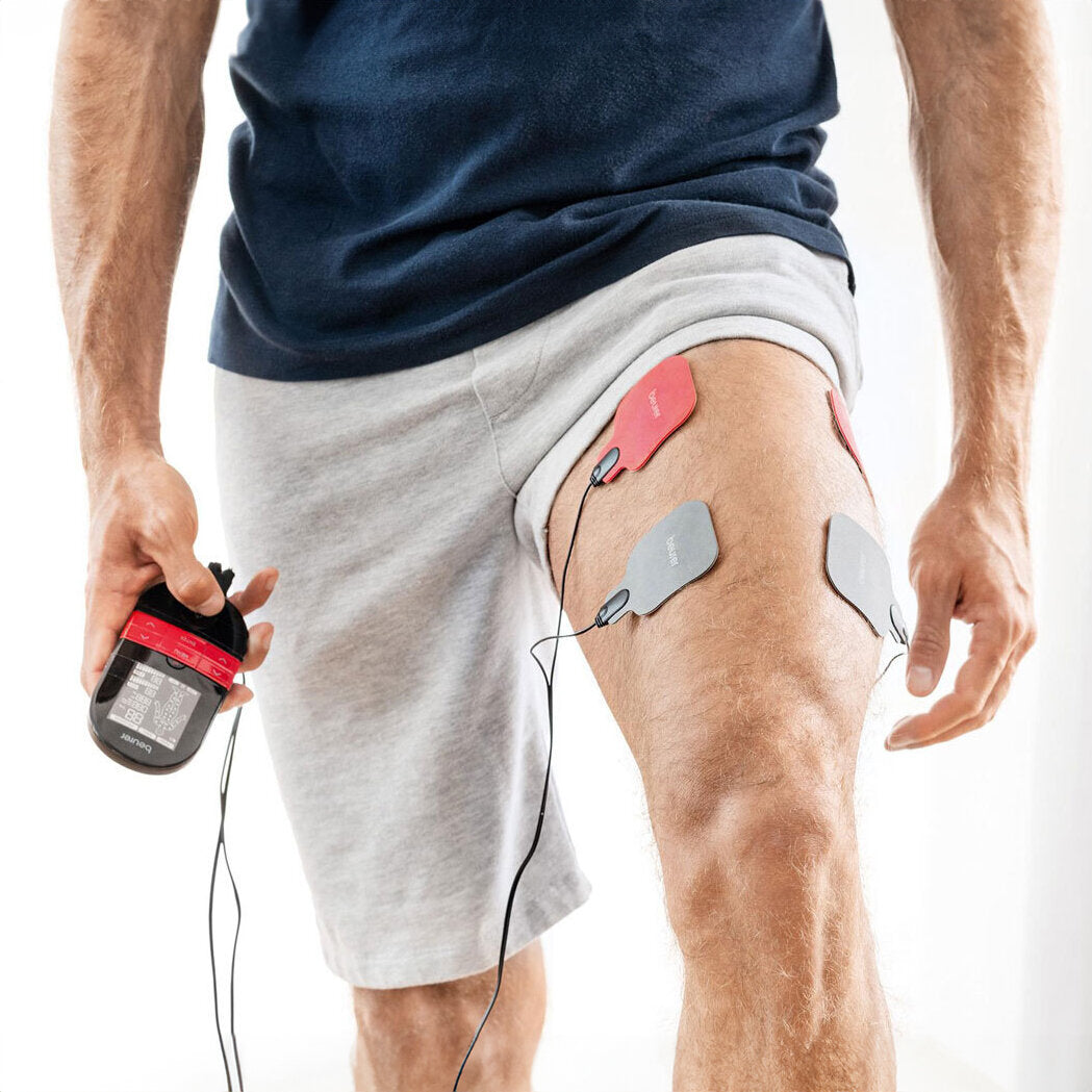 Mann mit EKG-Elektroden an Oberschenkel, hält EKG-Gerät in Hand, trägt Sportkleidung.