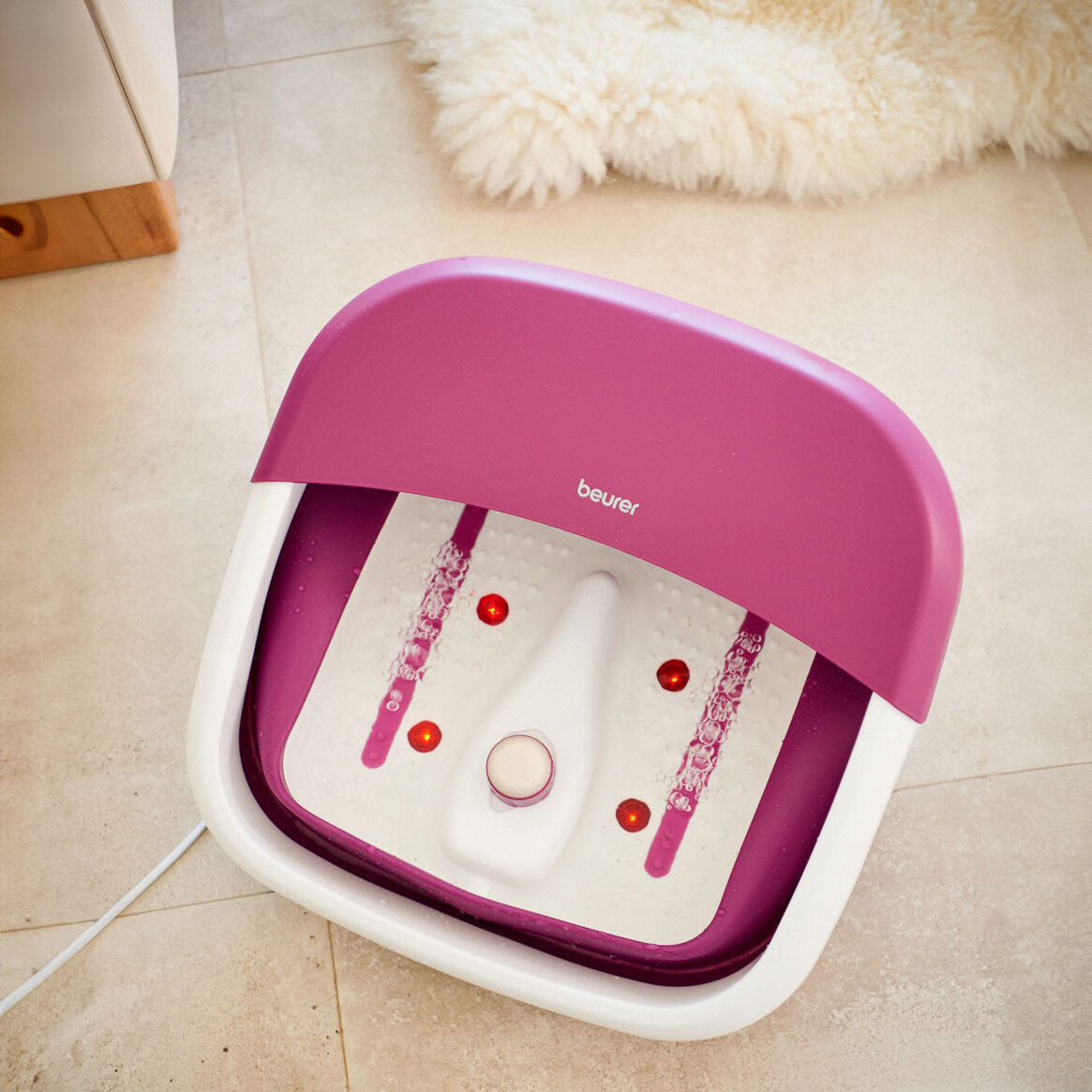 Fußbadewanne mit Wasser, Wasserstandsanzeige, rotem Licht, pinkem Deckel und weißem Boden.