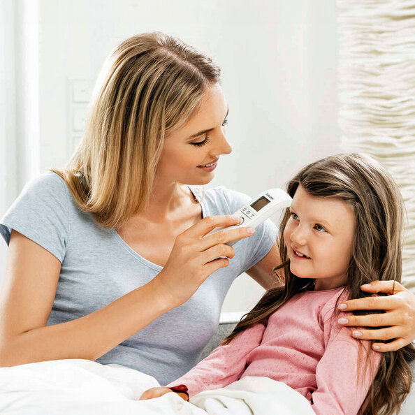 Frau misst bei einem Mädchen mit einem Fieberthermometer die Temperatur.