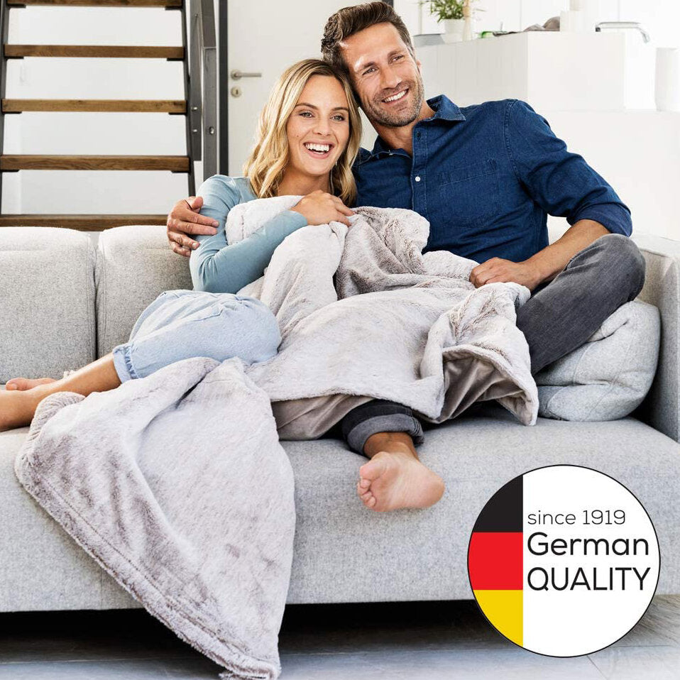 Ein lachendes Paar sitzt auf einem Sofa, die Frau ist schwanger, beide umarmen sich.