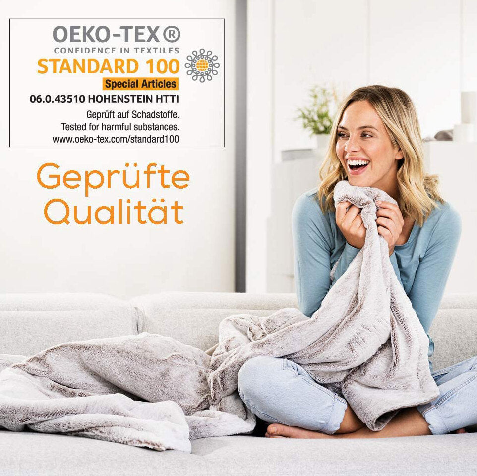 Frau sitzt auf Sofa, hält eine Decke, lächelt und schaut nach rechts. Text: "Geprüfte Qualität" und Zertifizierungsinformationen.