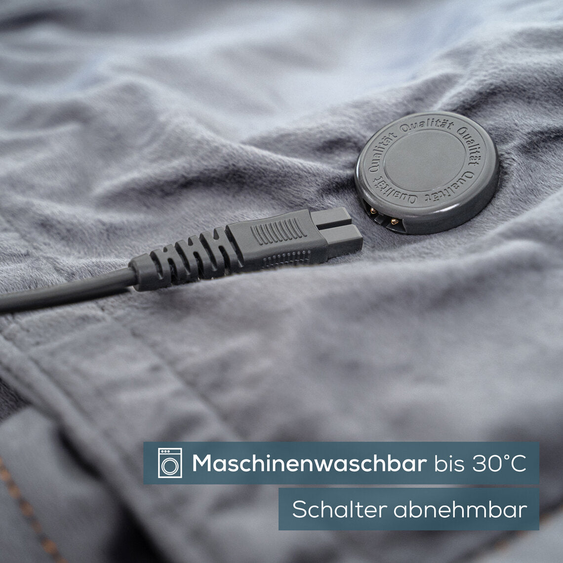 Stecker und runder Akku auf grauem Stoff, Text: "Maschinenwaschbar bis 30°C, Schalter abnehmbar".