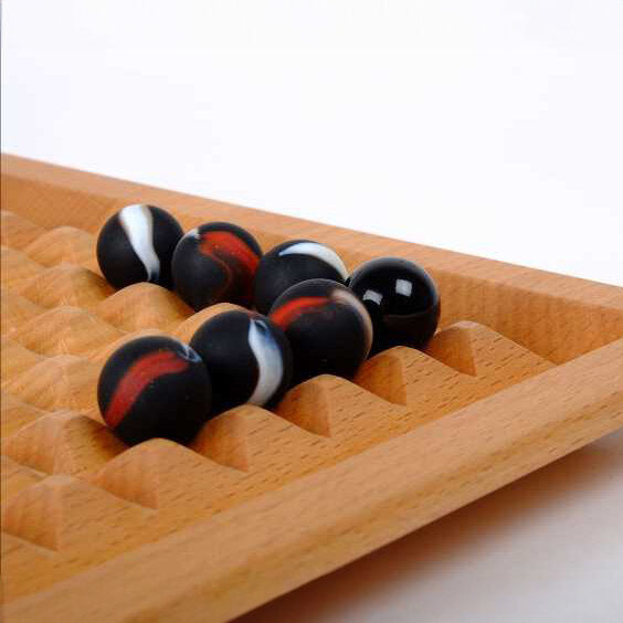 Holzspielzeug mit schwarzen, weißen und roten Kugeln in einer Holzmulde.