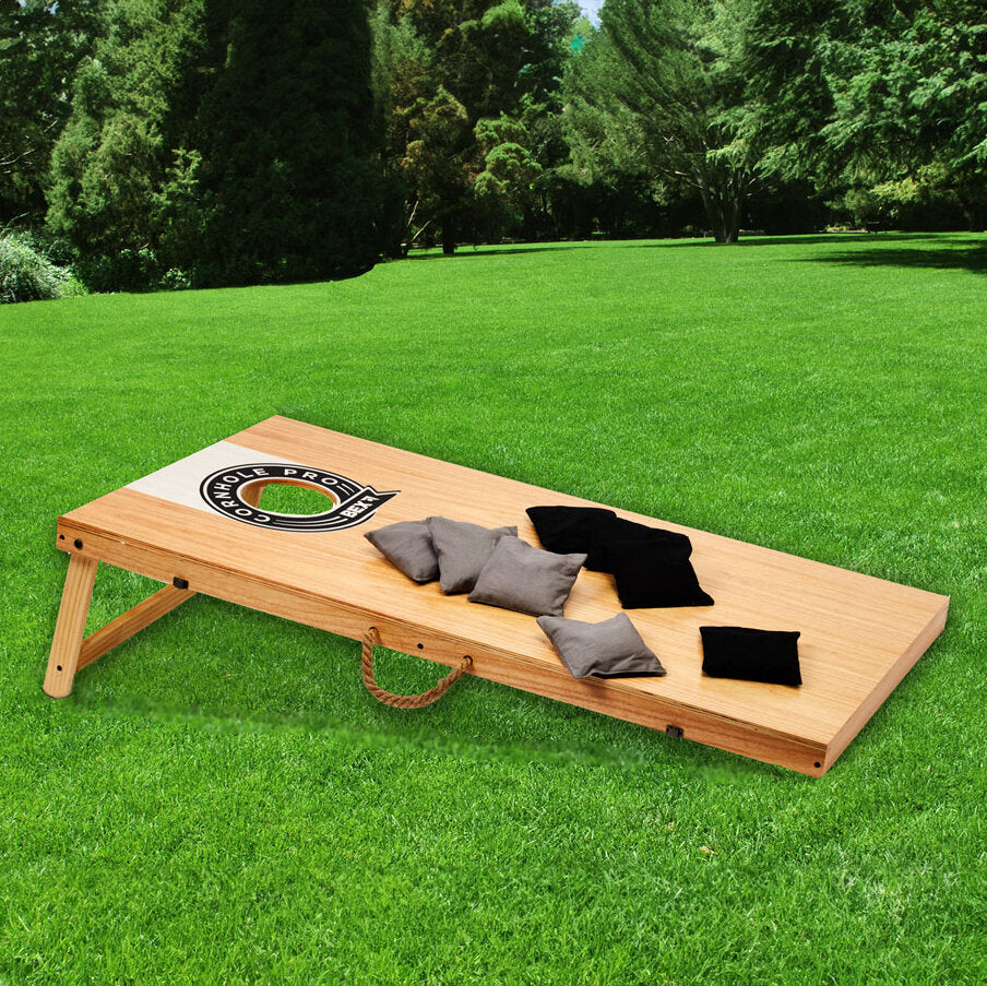 Ein Holz-Wurfbrett mit "Hole Pros" Logo und mehreren Socken liegt auf einer grünen Wiese.