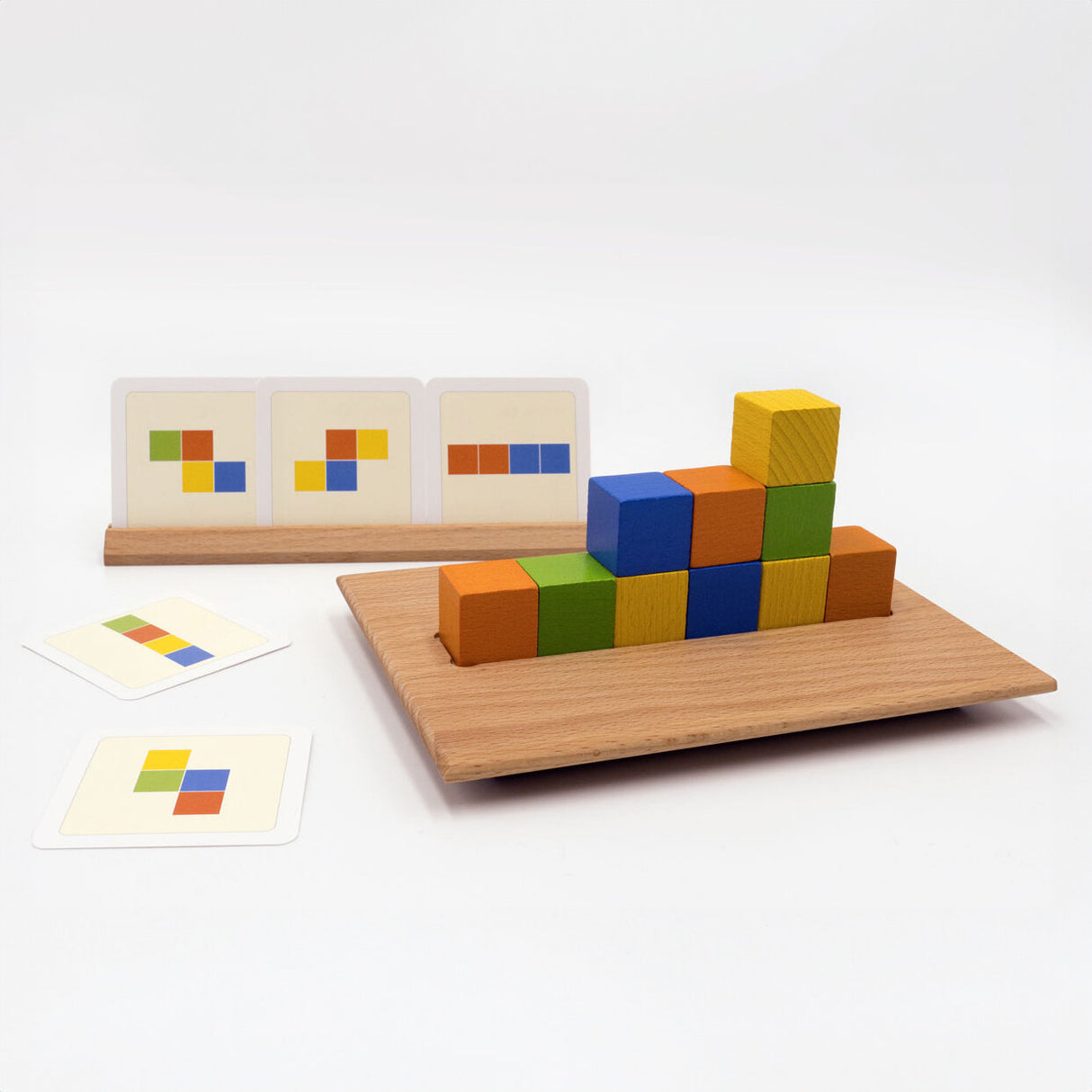 Bunte Holzbausteine auf einem Holzbrett, Karten mit Farbmustern im Hintergrund, Spielmaterial für Musterbildung.