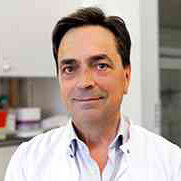 Porträt eines Mannes mit dunklem Haar, weißem Hemd, im Innenraum.