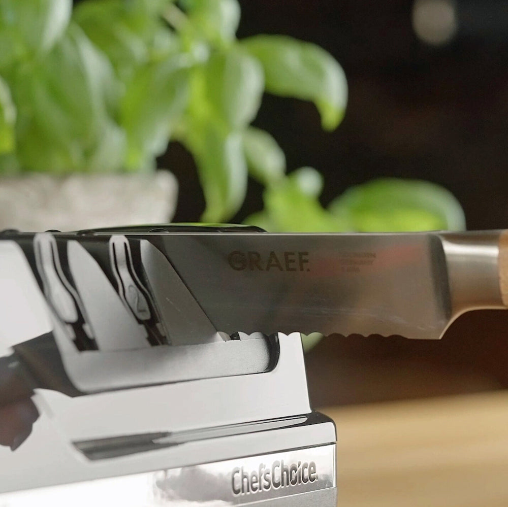 Küchenmesser mit "GRAEF"-Aufdruck, auf einem Messerblock mit "chefsChoice" Schrift, im Hintergrund grüne Pflanzen.