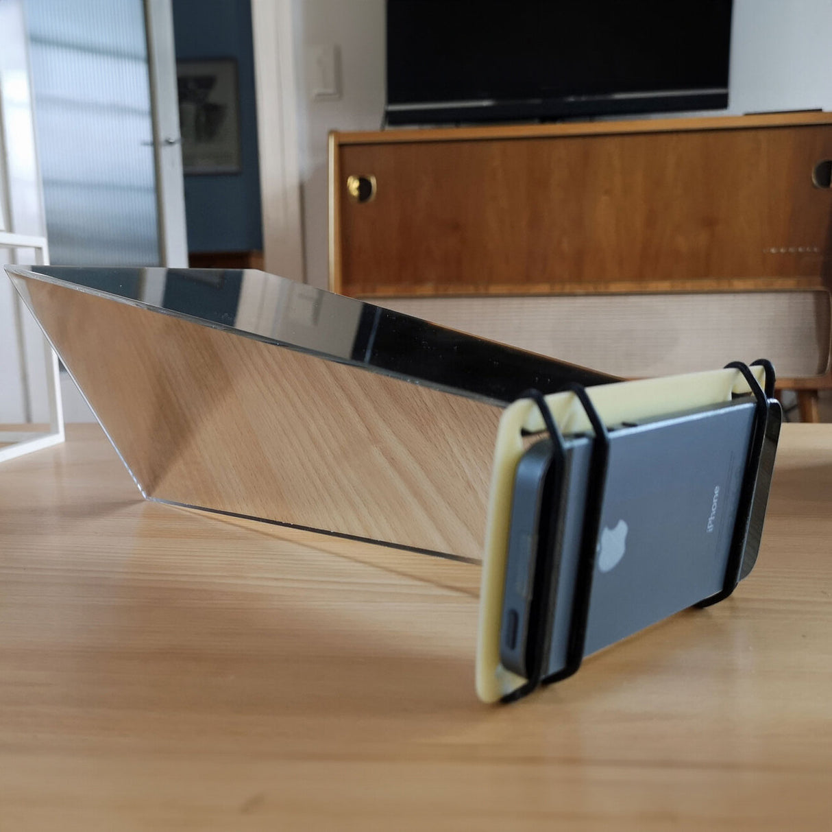 Smartphone in Silikonhülle, auf einem Holzständer, vor einem Spiegel auf einem Tisch.