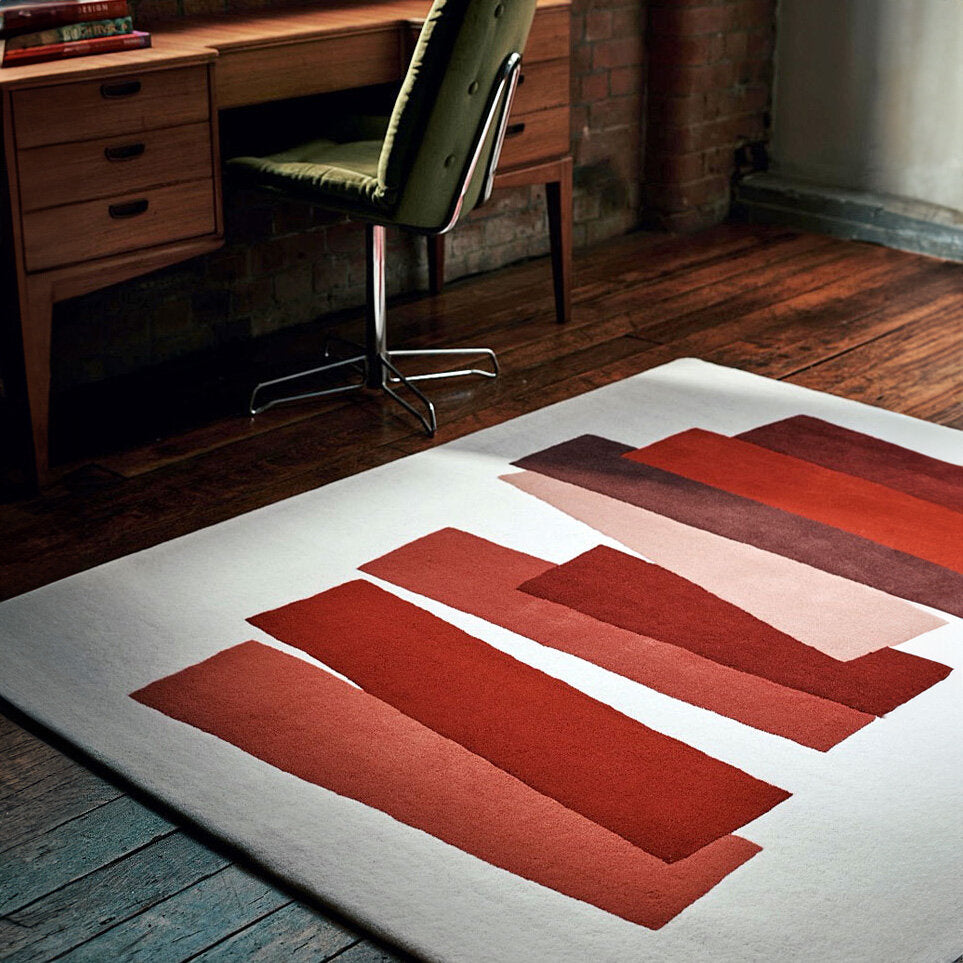 Roter, orange und rosa geometrische Muster auf einem weißen Teppich in einem Raum mit Holzfußboden und einem Schreibtisch.