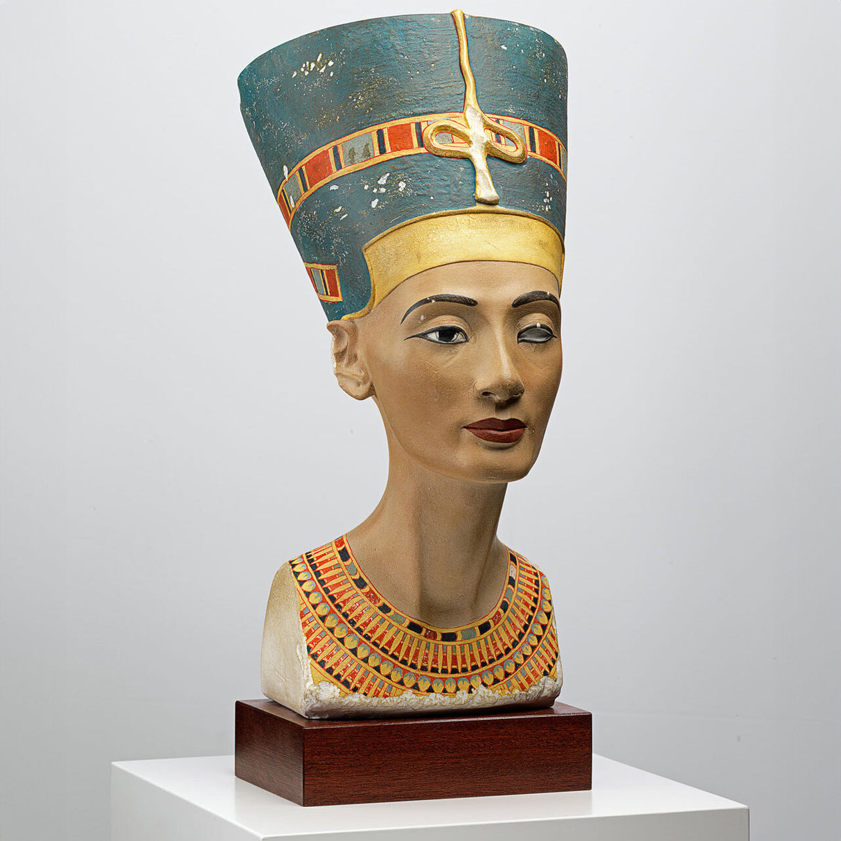 Statue eines ägyptischen Pharao-Kopfes mit kunstvoller Kopfbedeckung und Halskette auf Holzsockel.