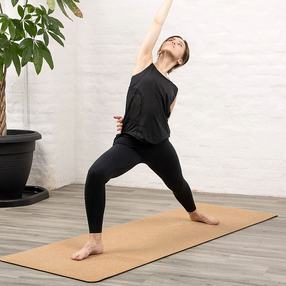 Frau macht Yoga auf einer Matte, hebt einen Arm nach oben und steht in einer weiten, seitlichen Dehnposition.