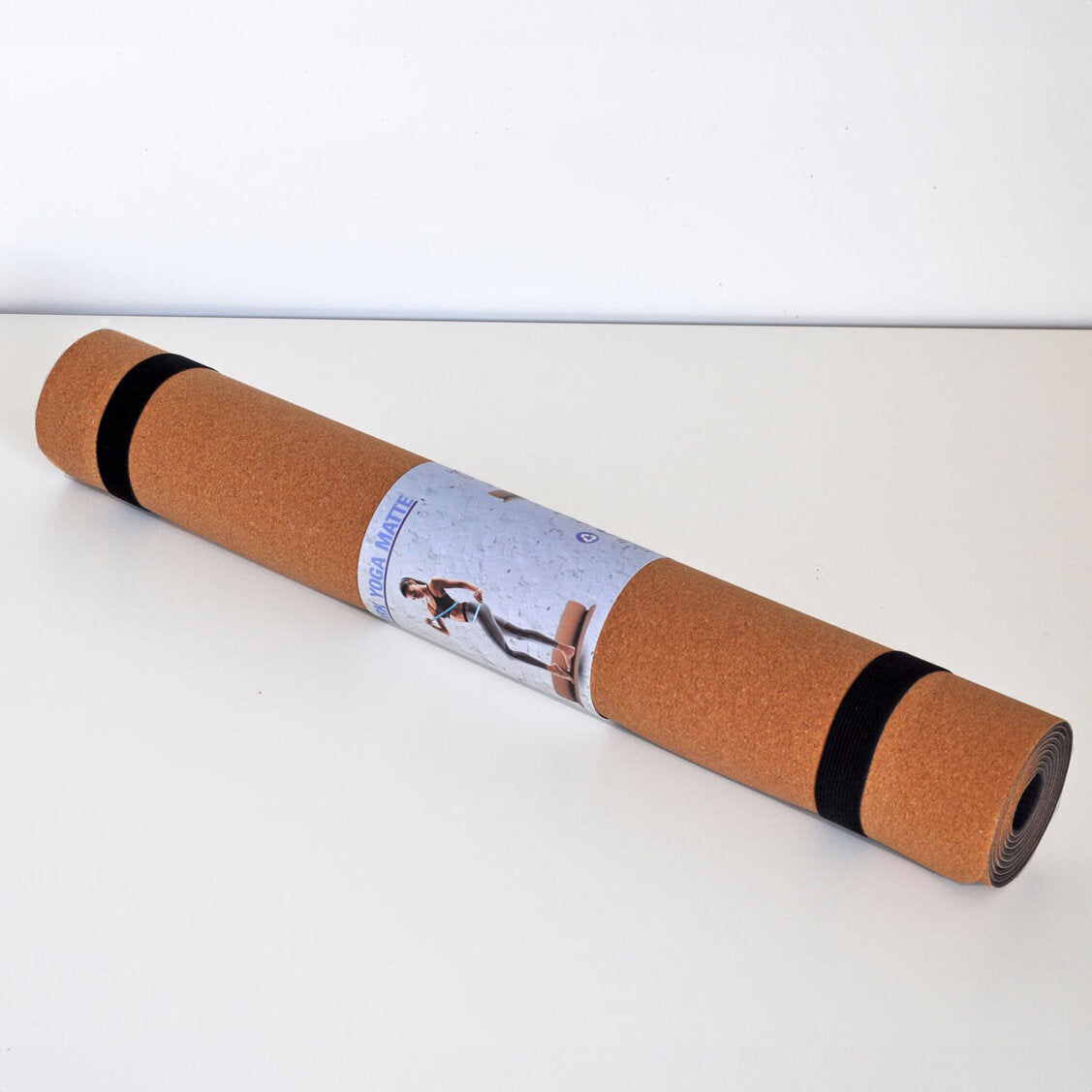 Yogamatte in Rolle mit schwarzem Band, auf weißem Tisch, mit Produktetikett.