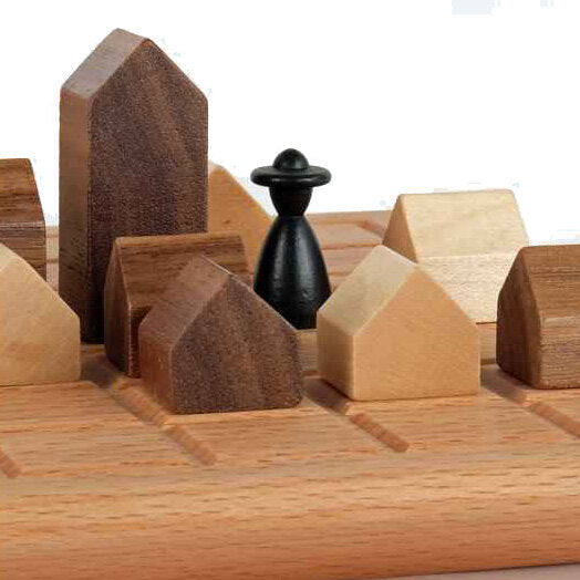 Holzspielzeug mit Häusern und einer schwarzen Spielfigur auf einem Holzbrett.