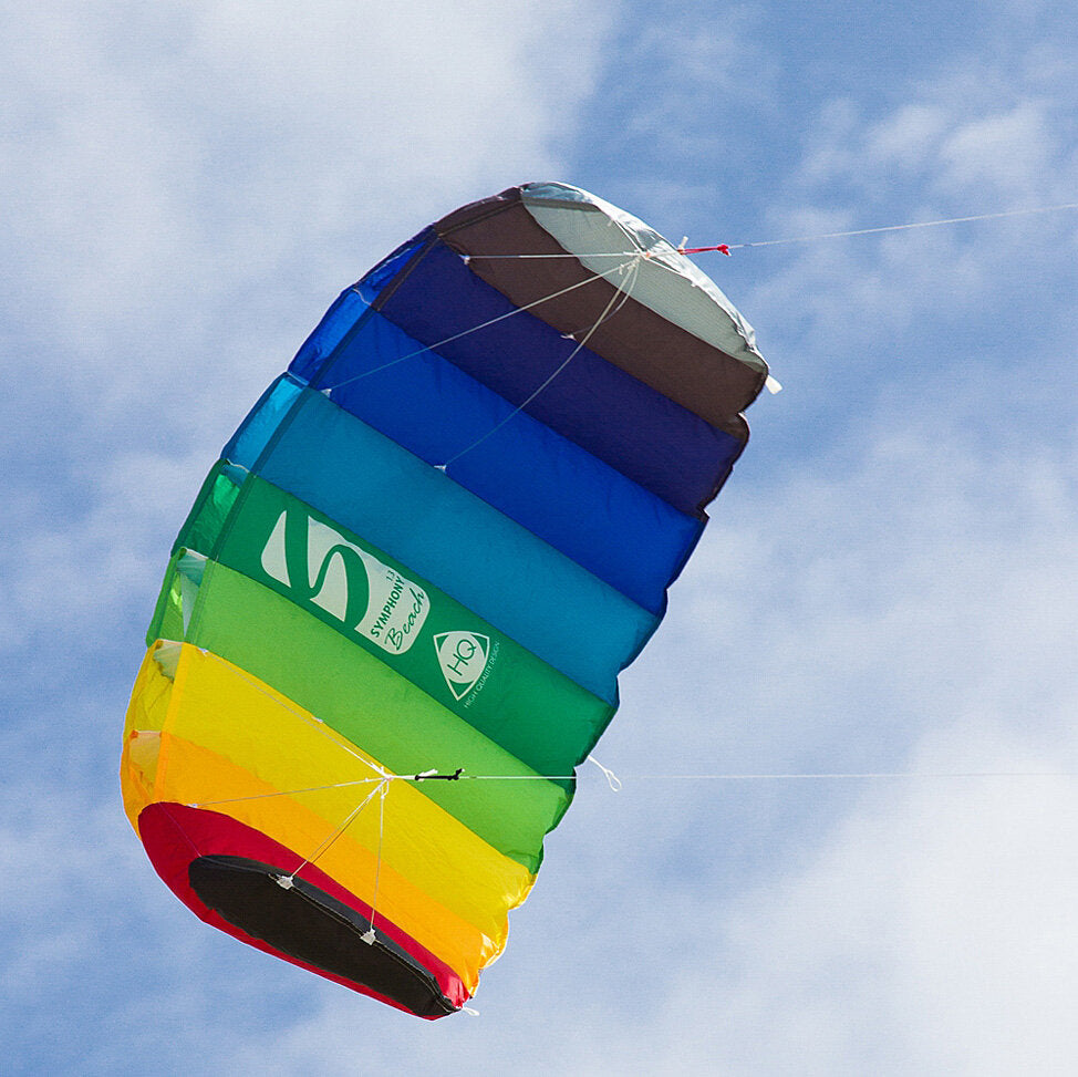Bunter, aufgespannter Drachen fliegt am Himmel mit blauer Wolkenhintergrund.