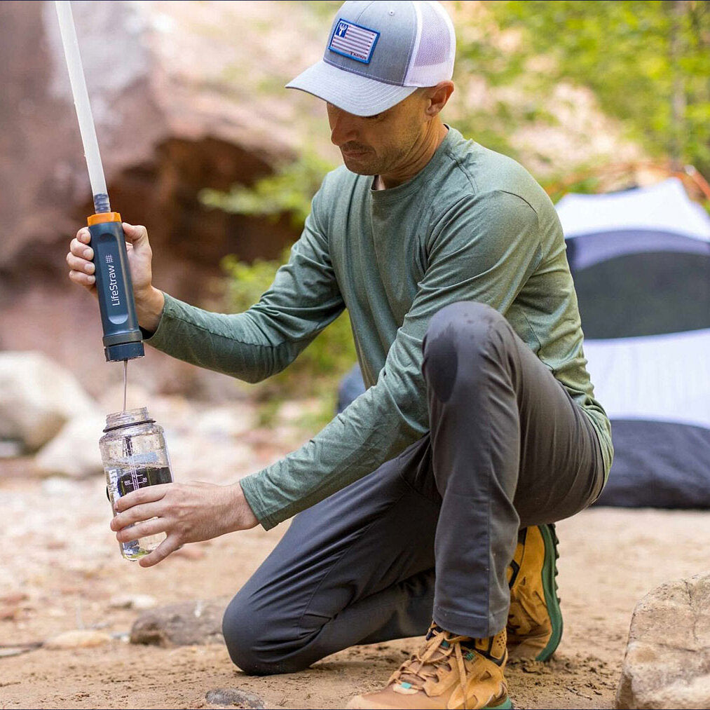 Mann mit Mütze und grünem Shirt hält einen LifeStraw in der Hand.