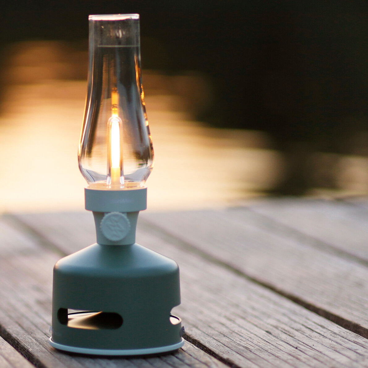Kleiner, batteriebetriebener LED-Glühbirne auf Holzterrasse bei Sonnenuntergang.