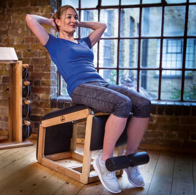 Schwangere Frau trainiert auf einem Pilates-Gerät in einem Fitnessstudio mit großen Fenstern und Holzfußboden.