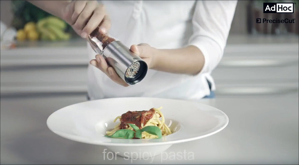 Person würzt Spaghetti mit Pfeffer über einem Teller Pasta.