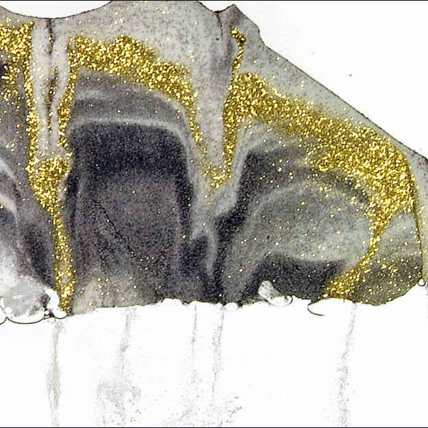 Schwarze und goldene Glitzerpartikel auf weißem Hintergrund, teilweise auf Papier.