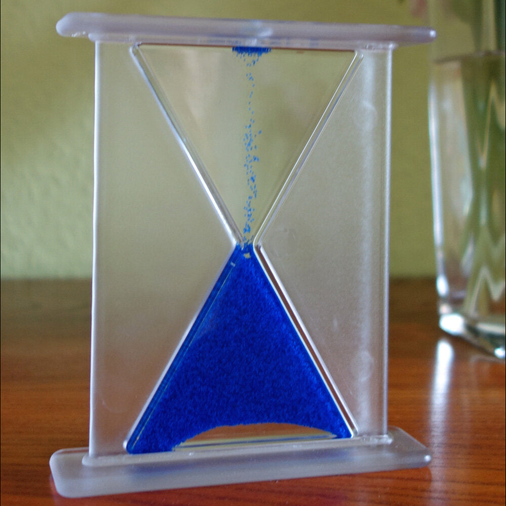 Sand läuft durch eine Sanduhr mit blauer Sandfüllung.