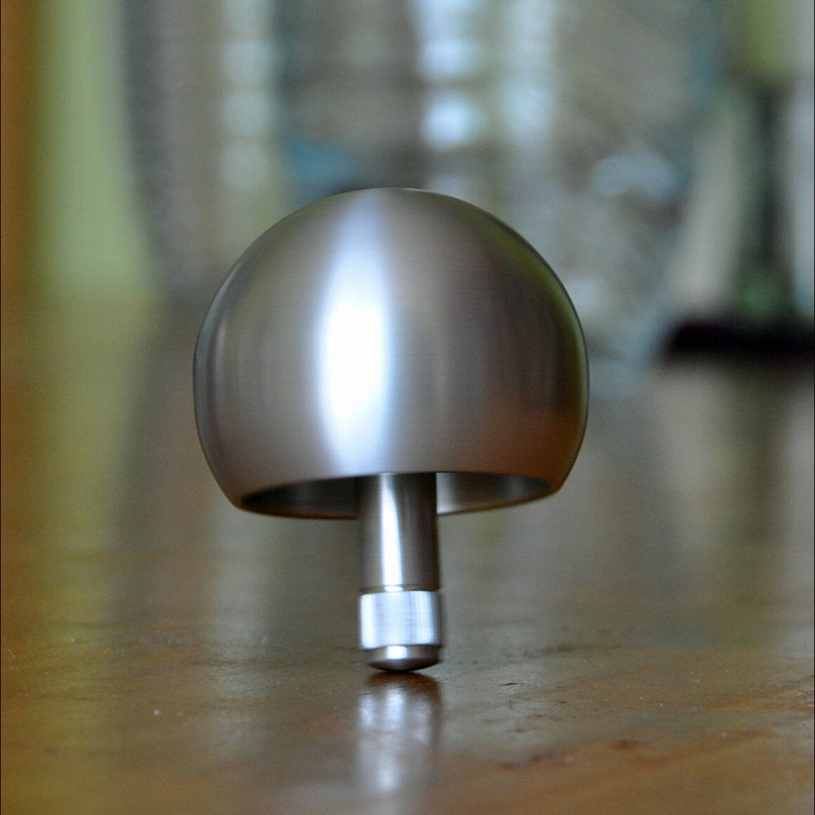 Silberner, runder Gegenstand auf einem Holztablett, mit einem kurzen Stiel, im Fokus, unscharfer Hintergrund.
