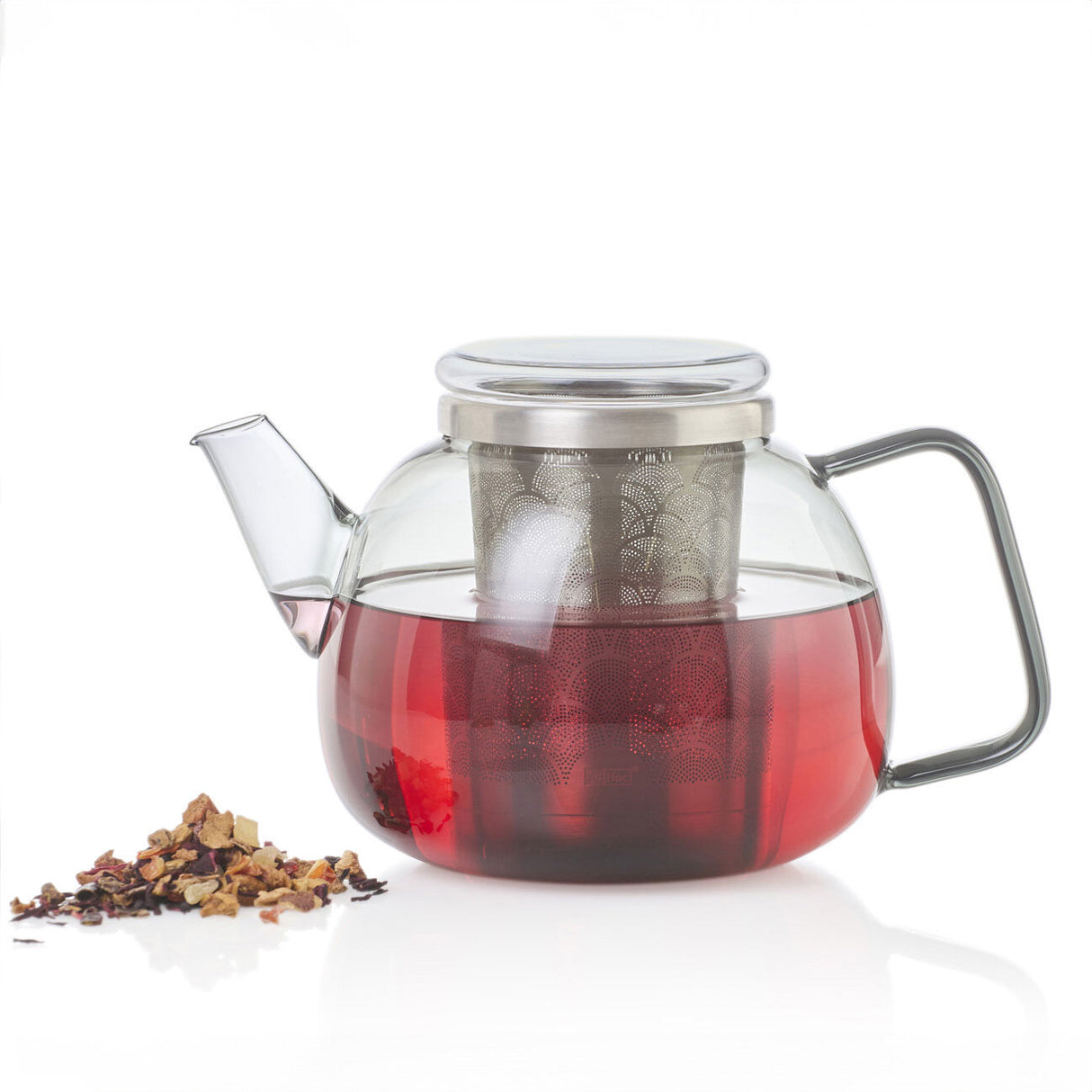 Glass teapot mit rotem Tee, Teesieb im Deckel, daneben lose Teemischung auf weißem Hintergrund.