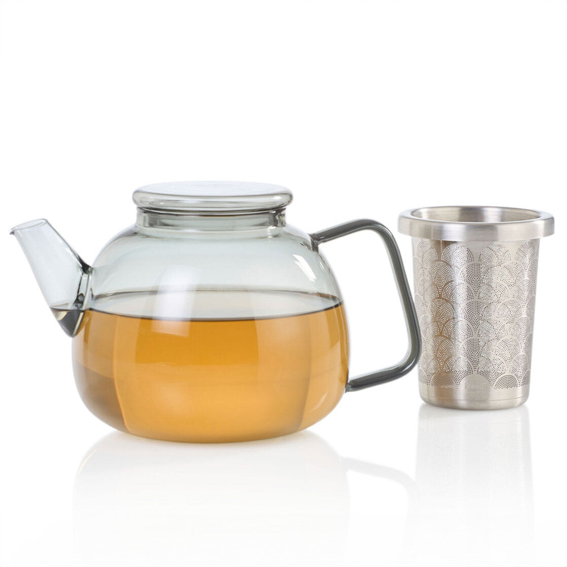 Glass-Kanne mit Tee und Metall-Teesieb daneben, auf weißem Hintergrund.
