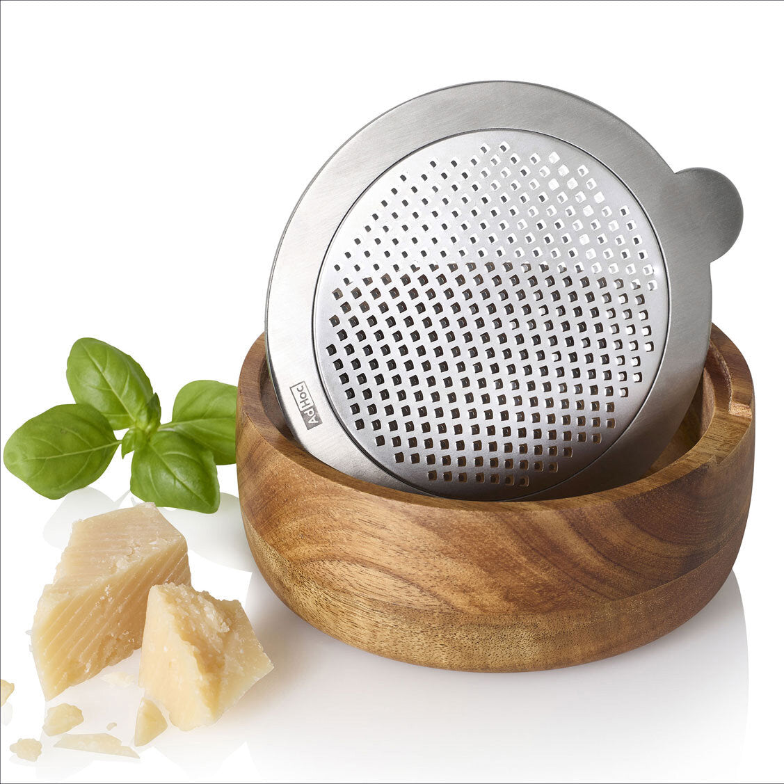 Käsemühle aus Edelstahl im Holzschälchen, neben Basilikum und Hartkäse.