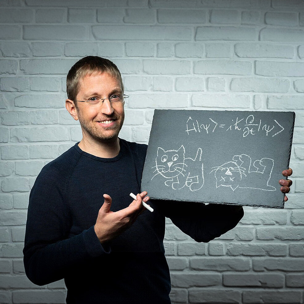 Mann hält Tafel mit mathematischer Formel und Katzenzeichnung vor weißer Ziegelwand.