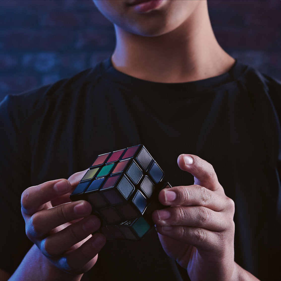 Person hält einen aufgerissenen Rubik's Cube in den Händen, dunkler Hintergrund, dunkles Oberteil.