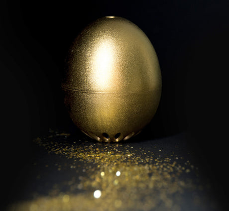 Goldene, ovale Schachtel mit Lochmuster, auf schwarzem Hintergrund, mit Goldstaub umgeben.