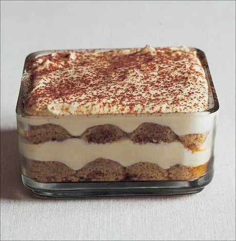 Schichtdessert in einer rechteckigen Glasform mit Cremeschichten und Kakaopulver oben.