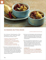 Zwei blaue Schalen mit gekochten schwarzen Linsen, daneben Knoblauch, Chili, Salz, und Gewürze auf einem Holztablett.