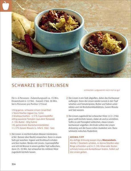 Zwei blaue Schalen mit gekochten schwarzen Linsen, daneben Knoblauch, Chili, Salz, und Gewürze auf einem Holztablett.