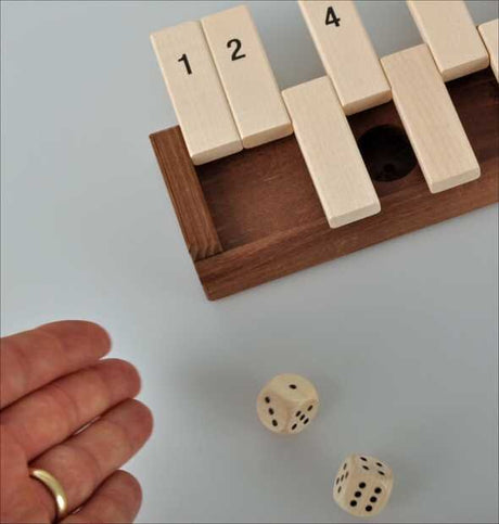 Holzblockpuzzle mit nummerierten Teilen, zwei Würfel mit Punkten, Hand mit Goldring.