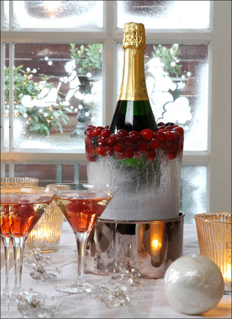 Sektflasche in Eiskübel mit roten Beeren, umgeben von Gläsern mit Rosé-Getränken, Kerzen und Dekorationen