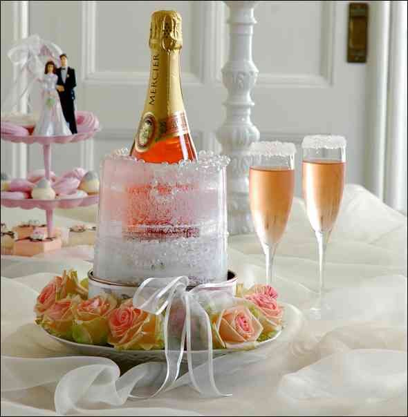 Flasche Sekt, zwei Sektgläser, Kuchen mit Schaum, rosa Rosen, Dekorationen, im Hintergrund eine Hochzeitstorte.