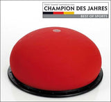 Rotes Balance- oder Gymnastikgerät auf schwarzem Kreis, mit Text und Logo oben.