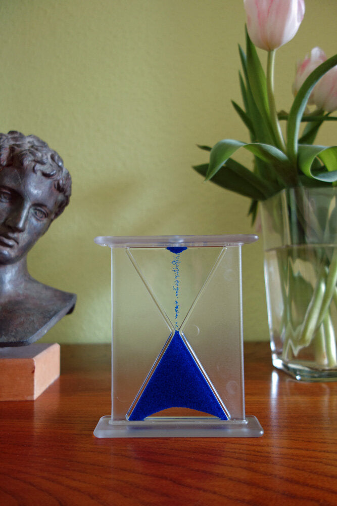 Sanduhr mit blauer Sandkörnern, daneben eine Bronzestatue und ein Blumenstrauß mit Tulpen in einer Vase.