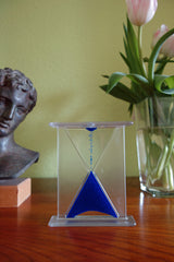 Sanduhr mit blauer Sandkörnern, daneben eine Bronzestatue und ein Blumenstrauß mit Tulpen in einer Vase.